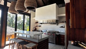 Cozinha moderna com uma ilha grande, eletrodomésticos de aço inoxidável e vista para o exterior.