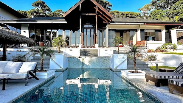 Uma área de piscina moderna com piscina azul cristalina, espreguiçadeiras e entrada coberta.
