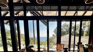 Um quarto espaçoso com grandes janelas, móveis de vime e vista para o mar.