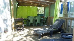 An outdoor patio with wooden decking, green chairs, and a covered seating area. - Découvrez le Camping Bois Soleil Dans le Confort de Notre Mobil Home ! (Saint-Georges-de-Didonne)