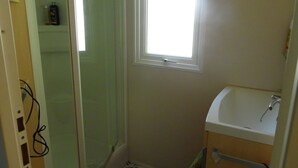 A small bathroom with a shower, a window, and a sink. - Découvrez le Camping Bois Soleil Dans le Confort de Notre Mobil Home ! (Saint-Georges-de-Didonne)