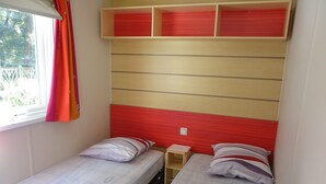 A small, compact room with two single beds, each with a pillow and a small bedside table. - Découvrez le Camping Bois Soleil Dans le Confort de Notre Mobil Home ! (Saint-Georges-de-Didonne)