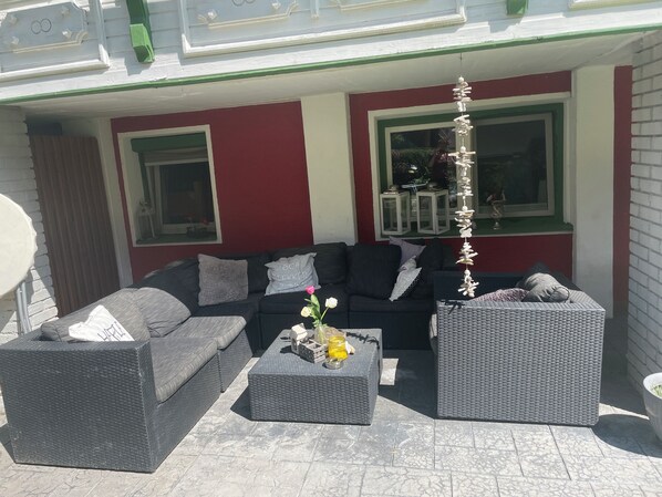 Een terras met een donkerbank en twee bijzettafeltjes, plus een decoratieve plantenopstelling.