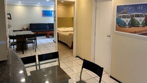 A hotel room with a dining area, a bed, and a painting of vintage vans on the wall. - Porto de Iracema Apartamentos (Fortaleza)