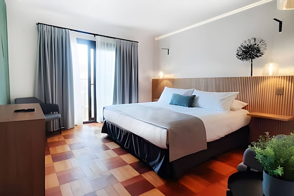 A modern hotel room with a large bed, a desk, and a potted plant.