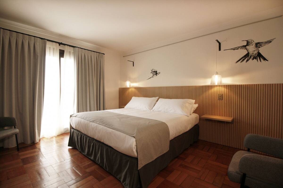 A neatly arranged bedroom with a large bed, a bedside table, a chair, and a wall-mounted light fixture.