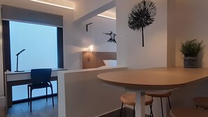 Et moderne hotelværelse med et stort vindue, et skrivebord med stol, et rundt bord med barstole og en potteplante.