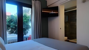 Et moderne hotelværelse med en stor seng, et fjernsyn monteret på væggen og en skydedør, der fører til et udendørs område.