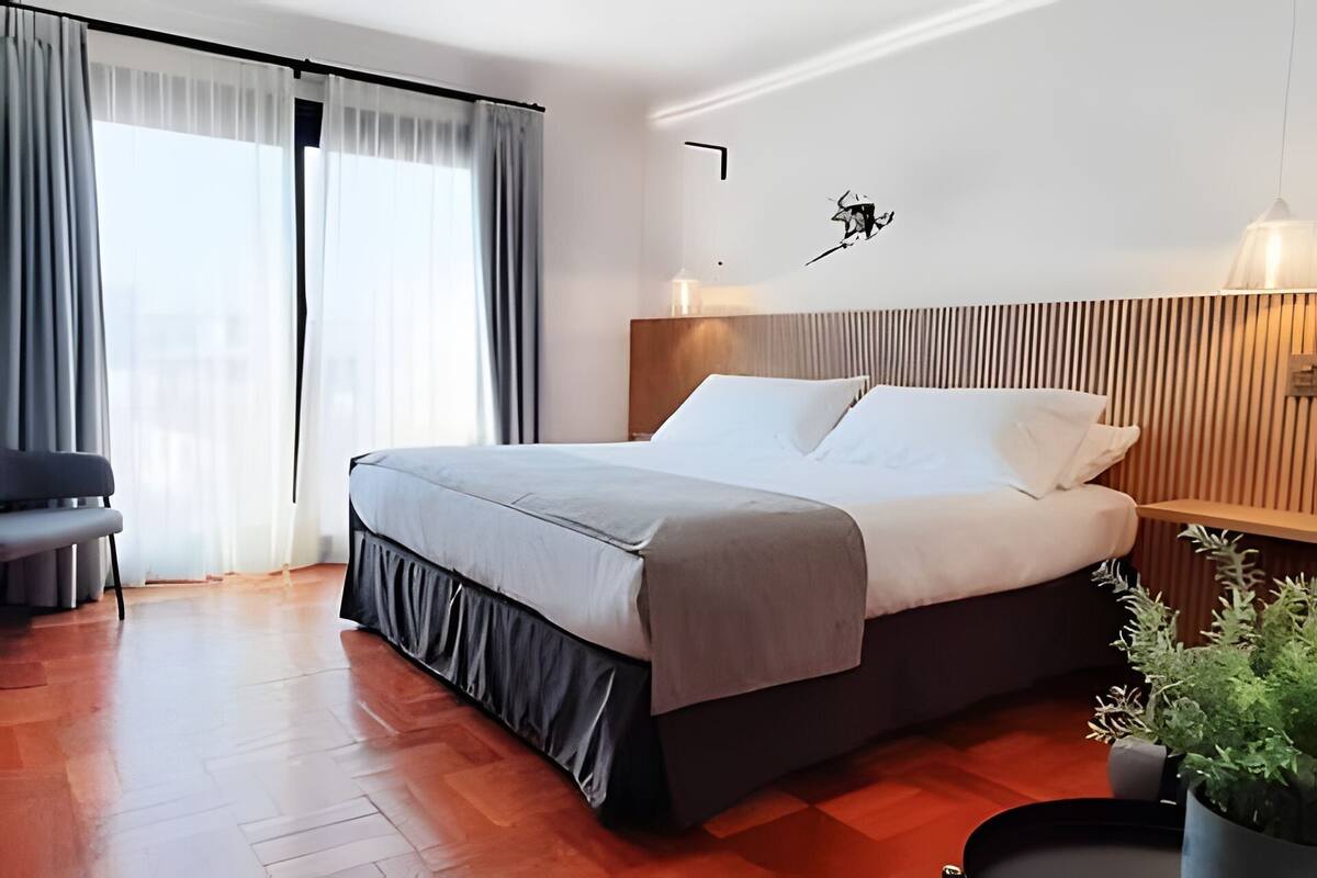 A modern hotel room with a large bed, a desk, and a potted plant.