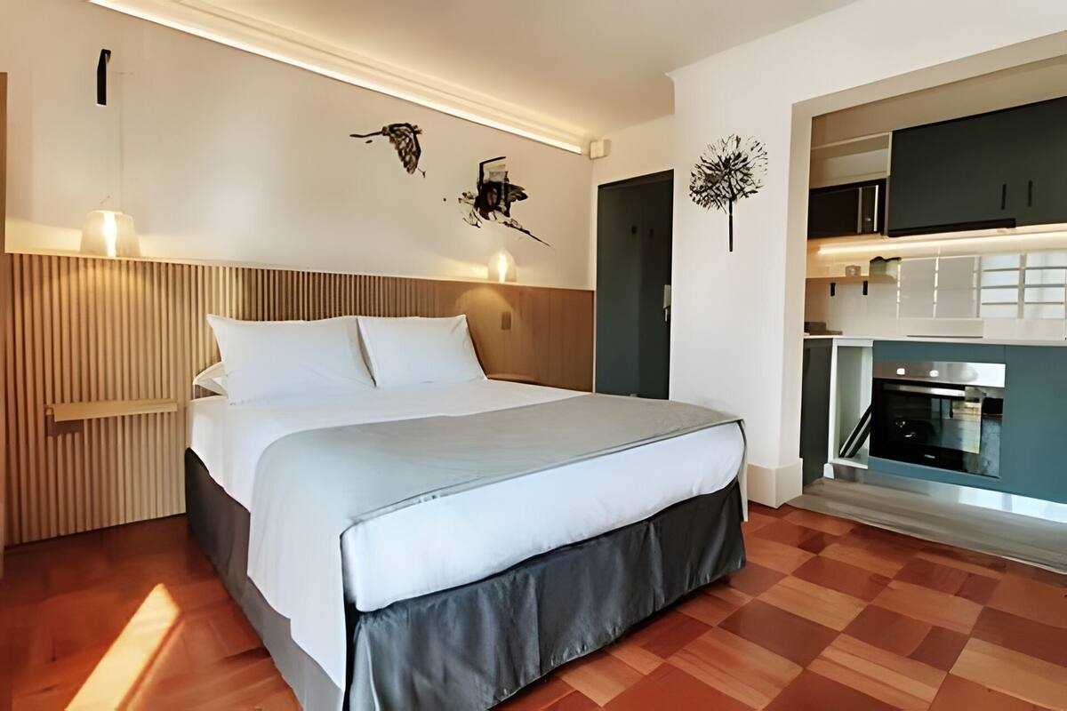 A modern bedroom with a wooden headboard, a large bed, and a kitchenette with a stove and microwave.