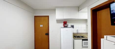 Una habitación pequeña con cama, kitchenette y puerta de madera.