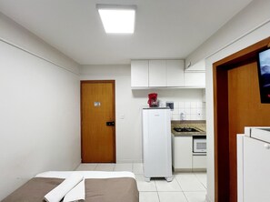 A compact room with a bed, a kitchenette, and a wooden door. - Residencial Carajás (Goiania)
