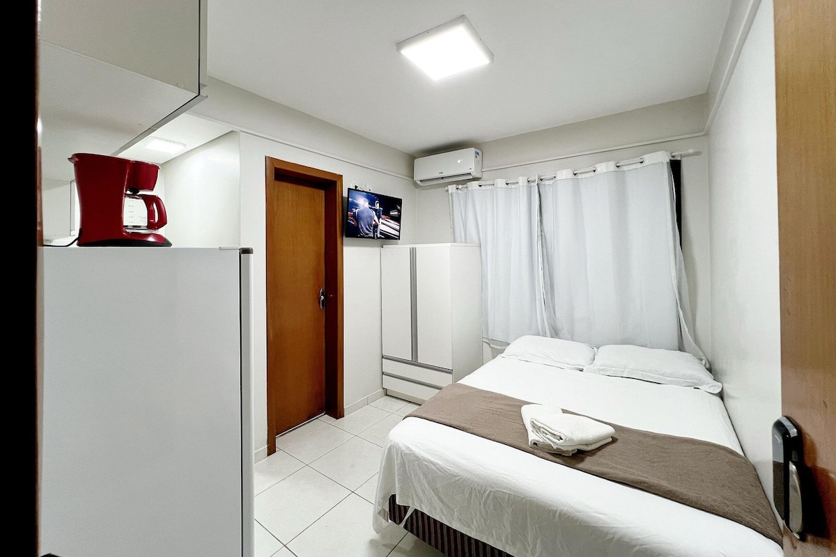 Quarto de hotel com cama, televisão, máquina de café e guarda-roupa.