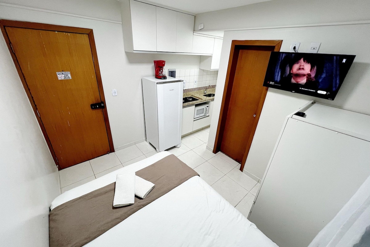 Quarto de hotel com cama, televisão, cozinha compacta e banheiro.