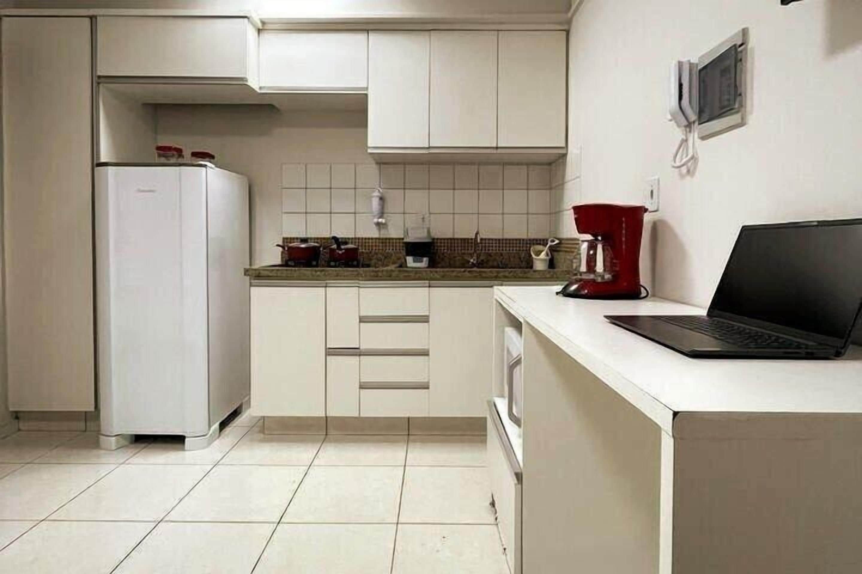 A kitchen with a white refrigerator, a microwave, a coffee maker, and a laptop on the counter.
