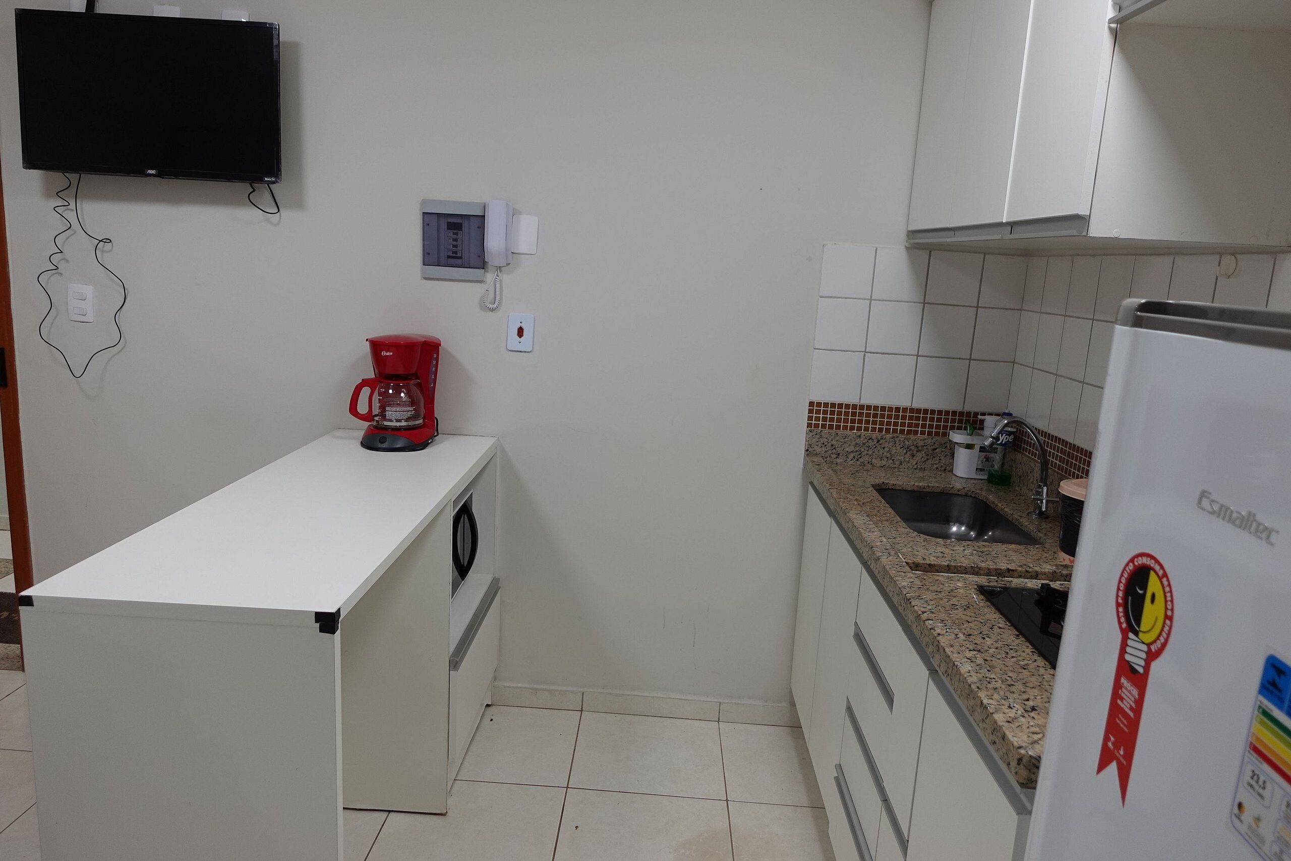 Una cocina con encimera blanca, cafetera roja, refrigerador blanco y teléfono de pared.