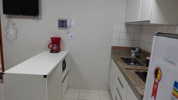 A kitchen with a white countertop, a red coffee maker, a white refrigerator, and a wall-mounted phone.