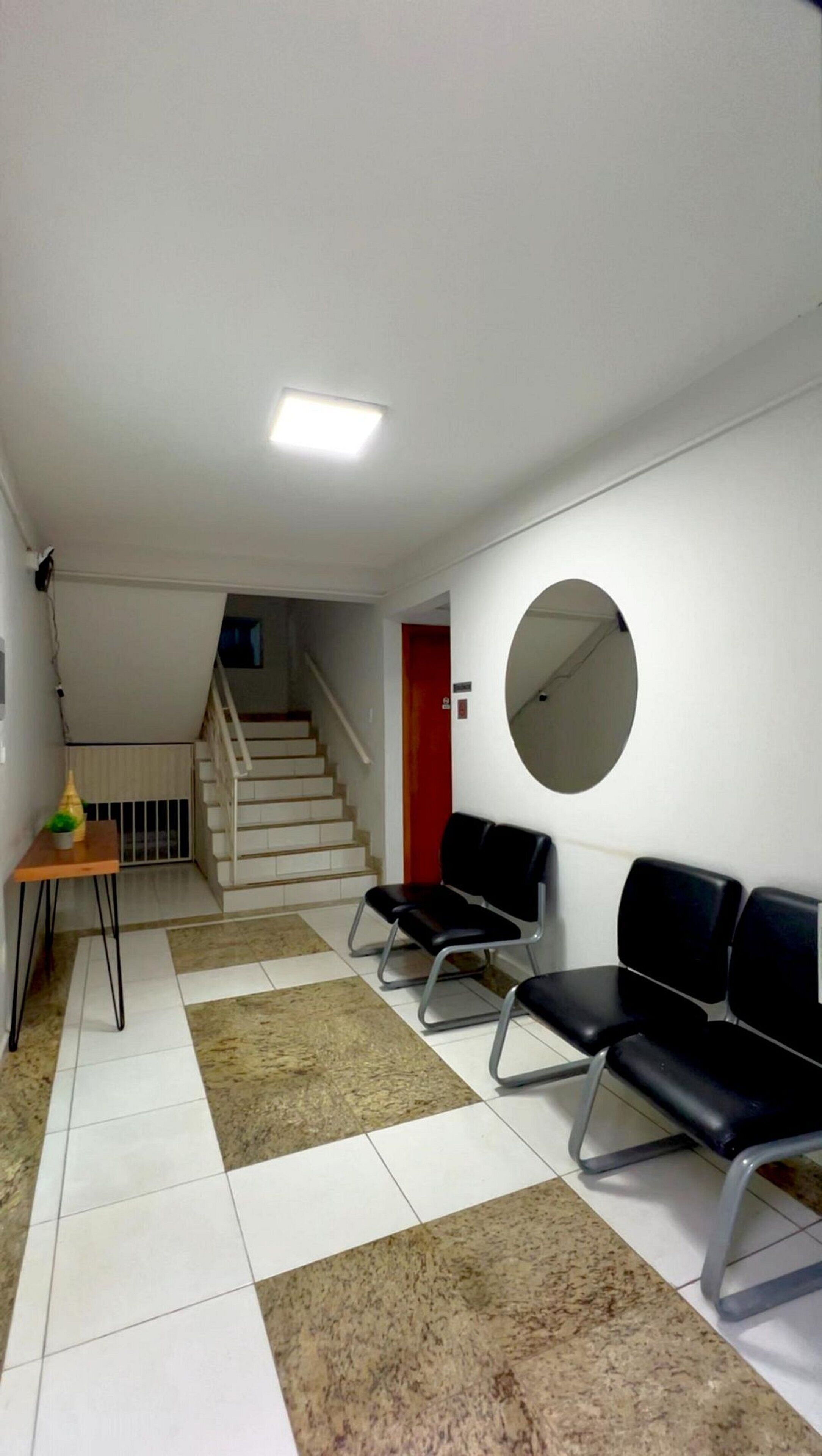 Un área de espera con una escalera, un espejo redondo y una mesa con un florero.