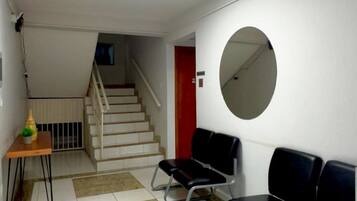 A waiting area with a staircase, a round mirror, and a table with a vase.