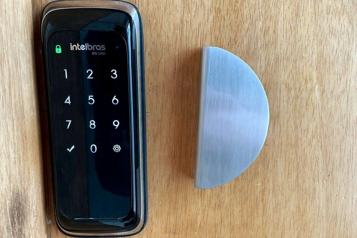 Um smartphone com teclado numérico e tela de bloqueio, apoiado em uma superfície de madeira ao lado de um objeto metálico.