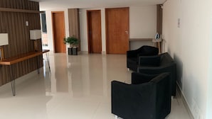 A modern hotel lobby with a reception desk, black seating, wooden doors, and a potted plant. - Residencial Carajás (Goiania)