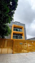 Un edificio moderno con fachada amarilla, entrada protegida por un portón y señalización que indica zona de entregas.