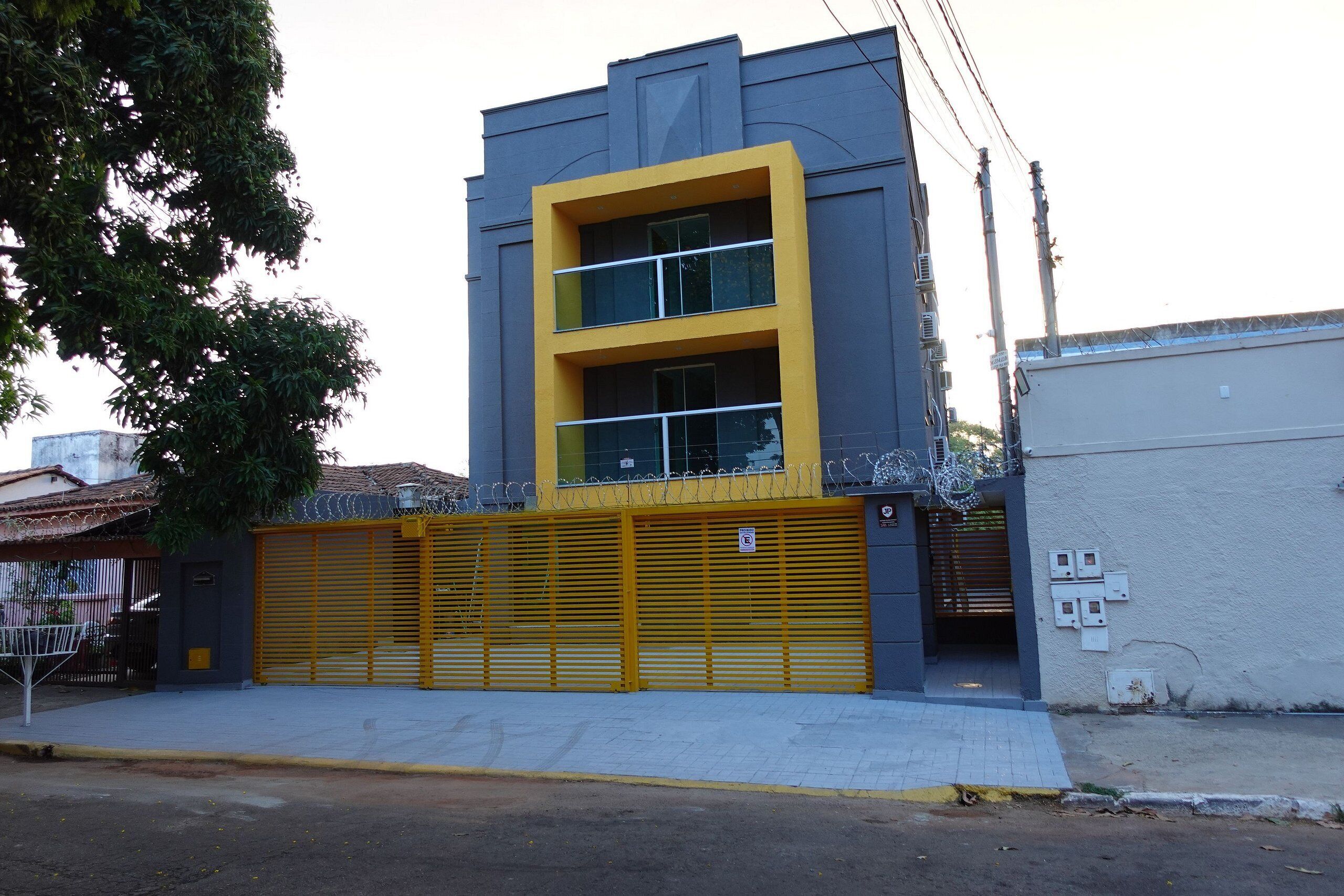 Un edificio con puerta de garaje amarilla, fachada gris y una ventana con barandilla de metal.