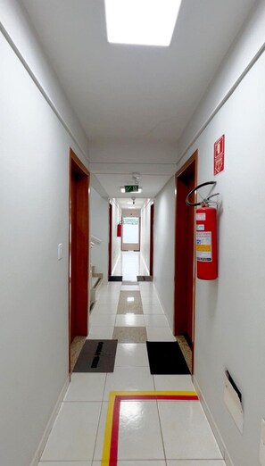 Un pasillo con un extintor, una puerta roja y suelo de baldosas.