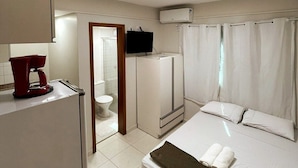A hotel room with a bed, a TV, a coffee maker, and a shower area. - Residencial Carajás (Goiania)