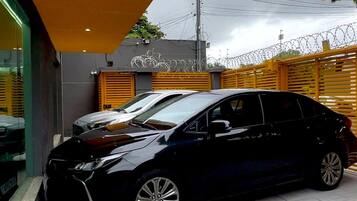 Un coche negro estacionado en un aparcamiento con un edificio amarillo y una valla con alambre de púas.