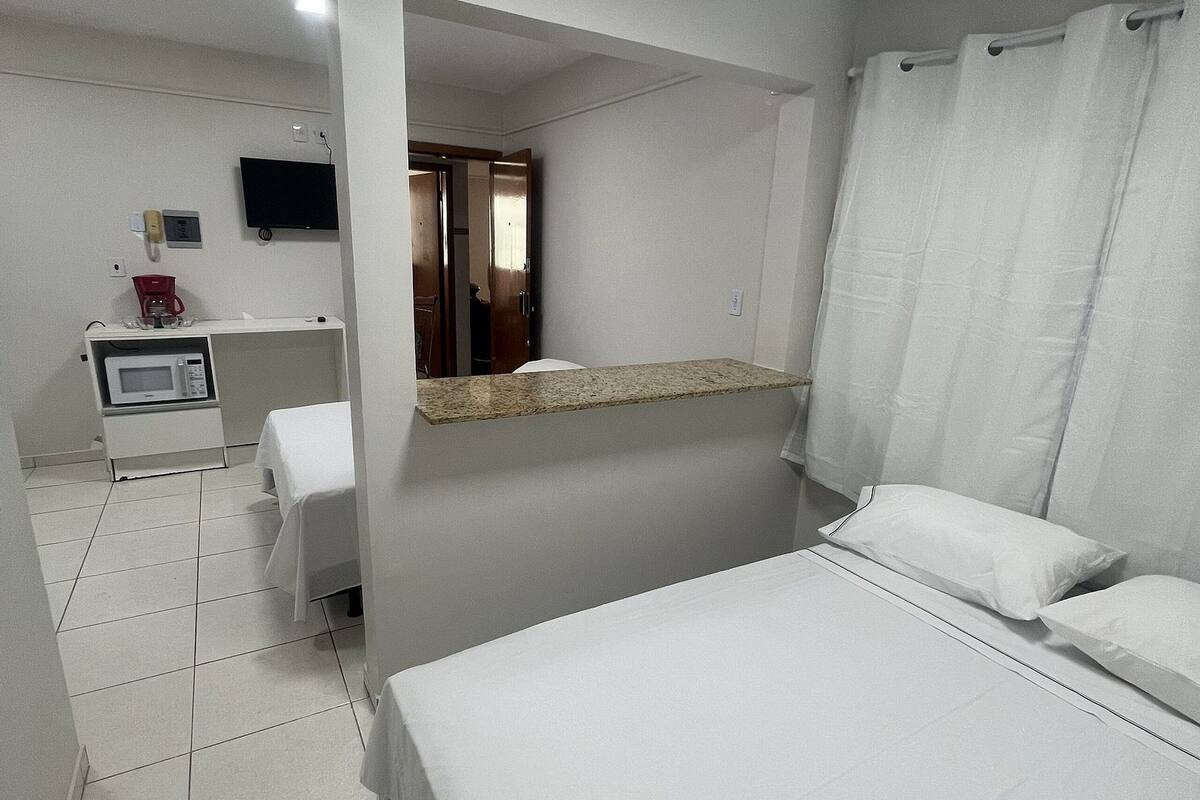 Quarto de hotel com cama, pequena mesa com micro-ondas, televisão e cortina de chuveiro.