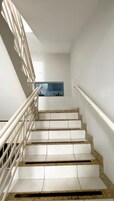 Una escalera con barandillas y escalones blancos que lleva a una habitación con ventana y pared azul.