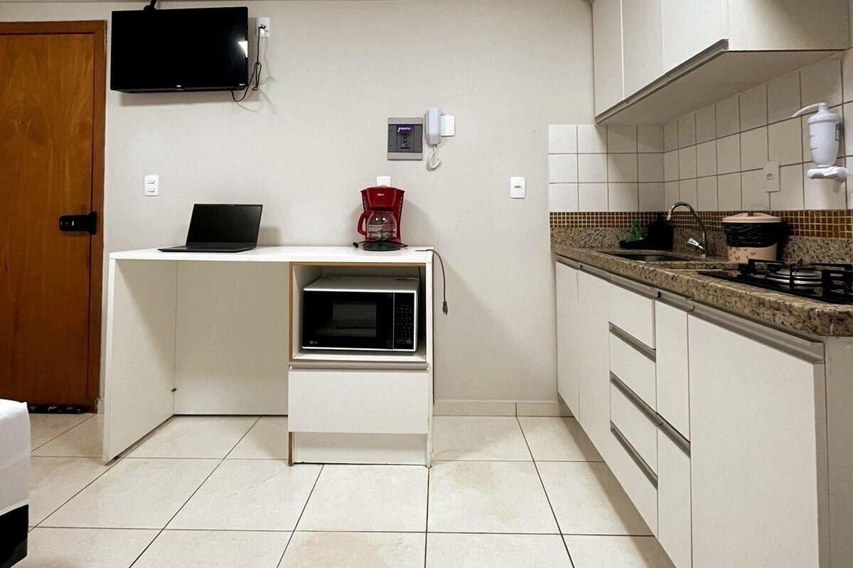 Una cucina compatta con forno a microonde, macchina del caffè e TV montata sopra il bancone.