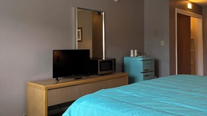 A hotel room with a bed, a television, a microwave, a dresser, and a door leading to another room. - Grand Lake Hotel (Lebanon)