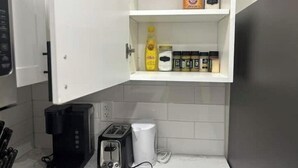 A kitchen with a coffee maker, toaster, and a shelf with condiments. - Guest Suite - Cozy Crib (Regina)