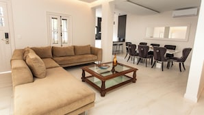 A modern living room with a sectional sofa, a glass-top coffee table, and a dining area with dark chairs and a white table. - LUXURY HOUSE VILLA DEVOTO (Buenos Aires)