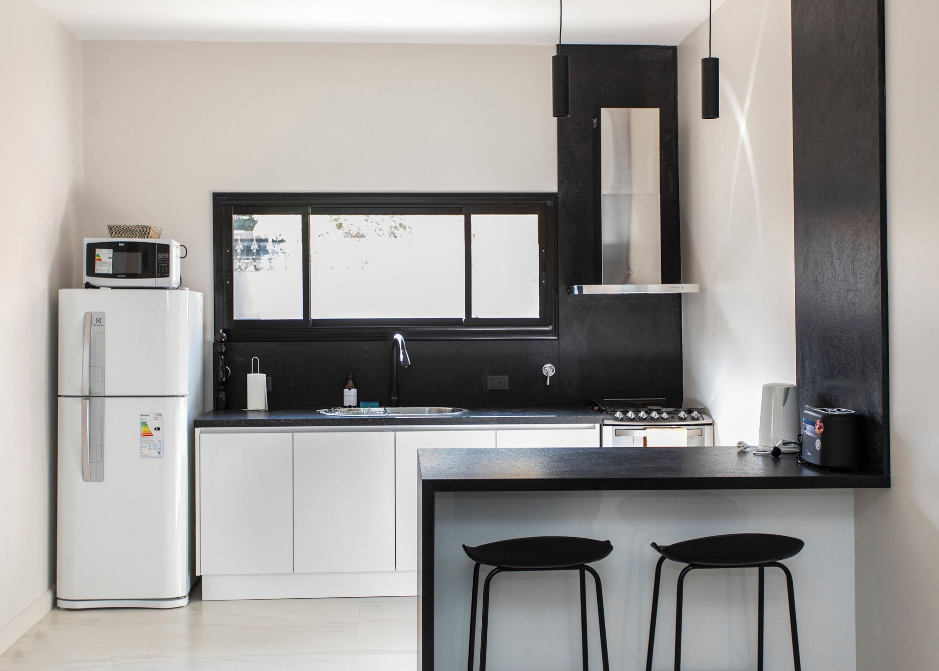 Eine kleine Küche mit Kühlschrank, Mikrowelle, Spüle, Herd und zwei Barhocker.