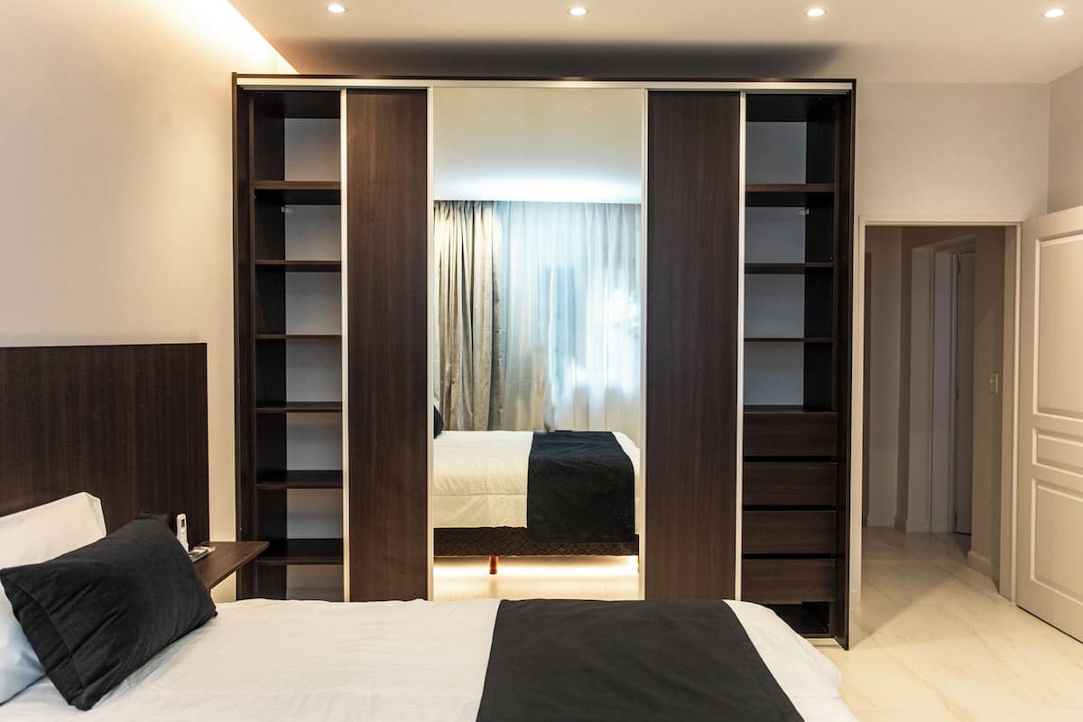 A modern hotel room with a large bed, a nightstand, and a wardrobe with multiple shelves.