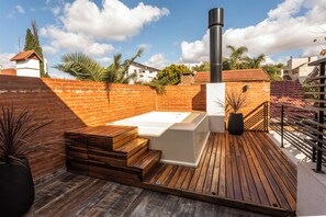 Eine Dachterrasse mit Whirlpool, Holzstufen und einer Backsteinmauer.