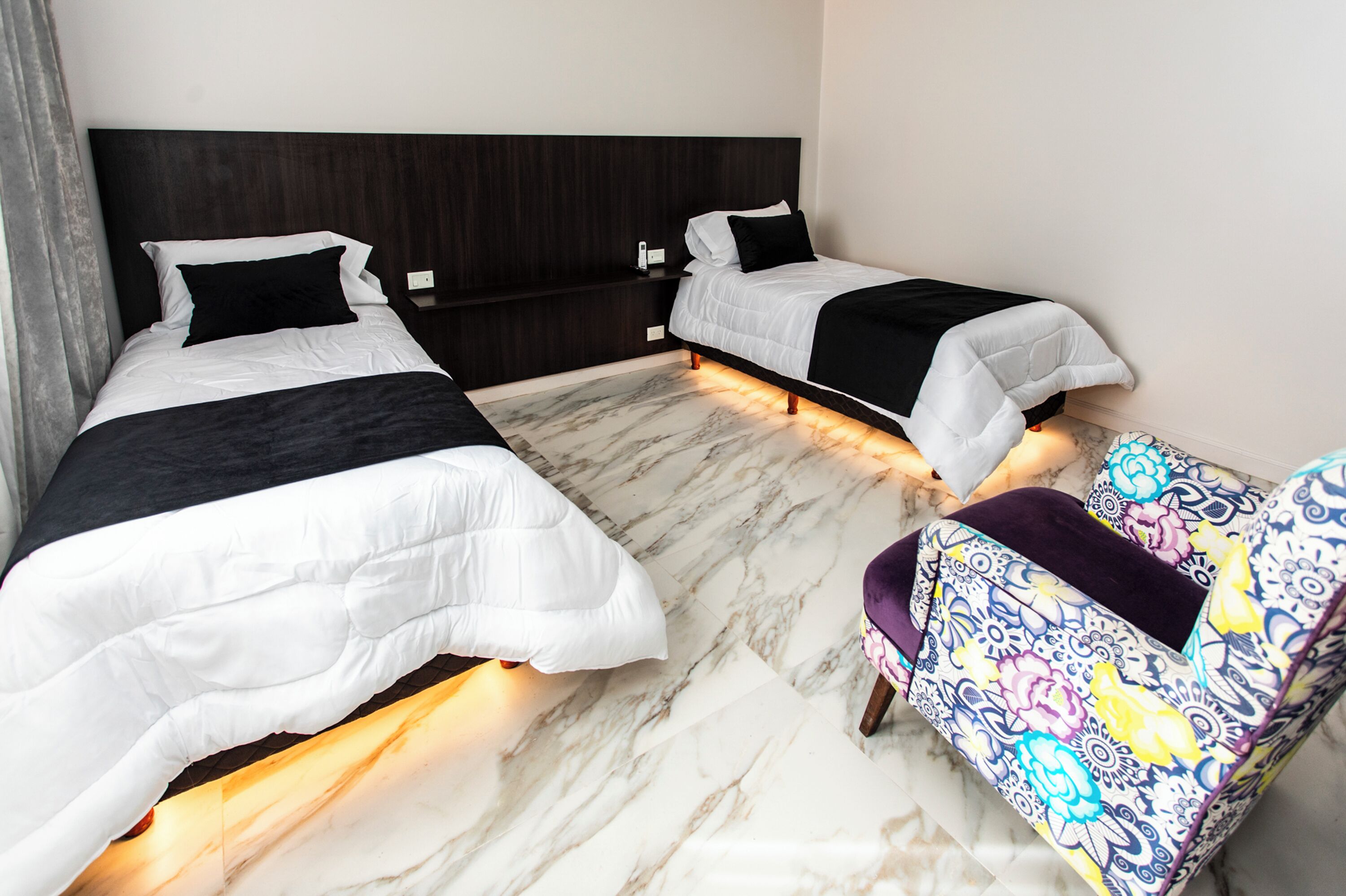 A hotel room with two beds, a nightstand, a chair, and marble flooring.