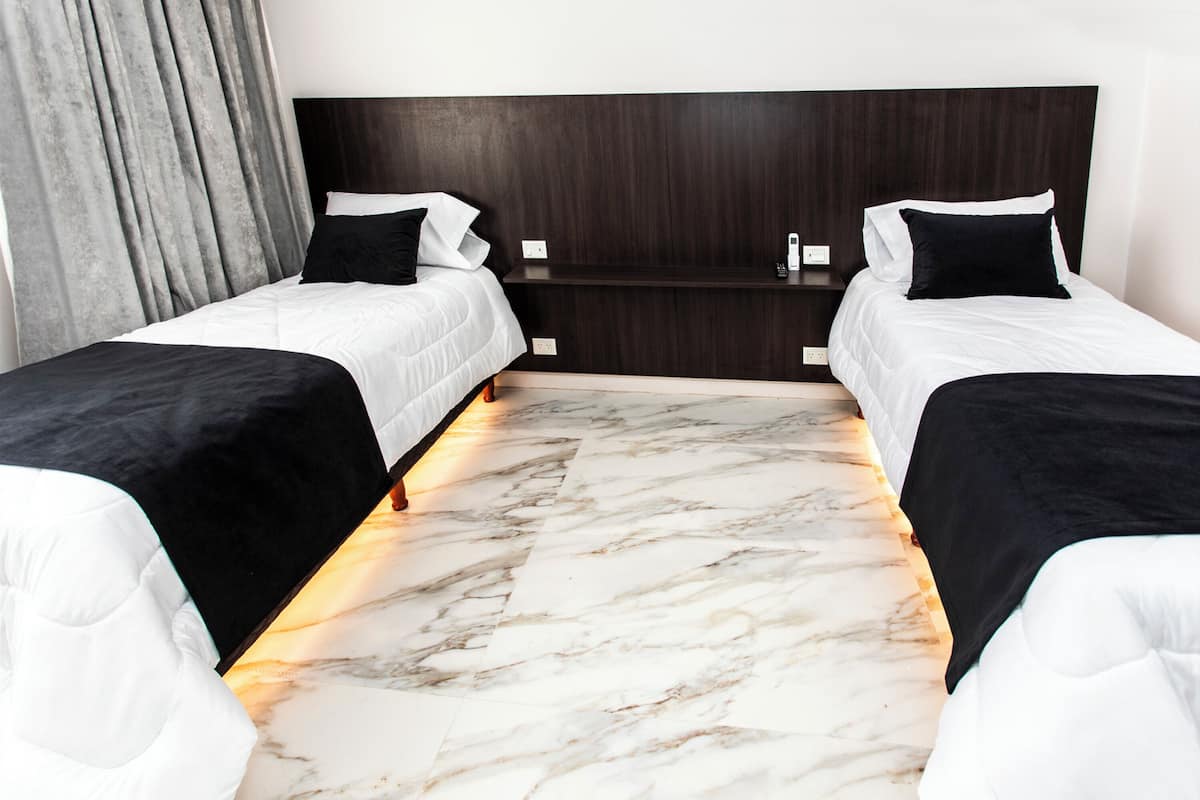 A hotel room with two single beds, a dark wood headboard, a marble floor, and a grey curtain.