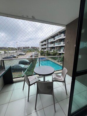 A balcony with a pool view, a table, and two chairs. - Makia Beach Experience Porto de Galinhas (Ipojuca)