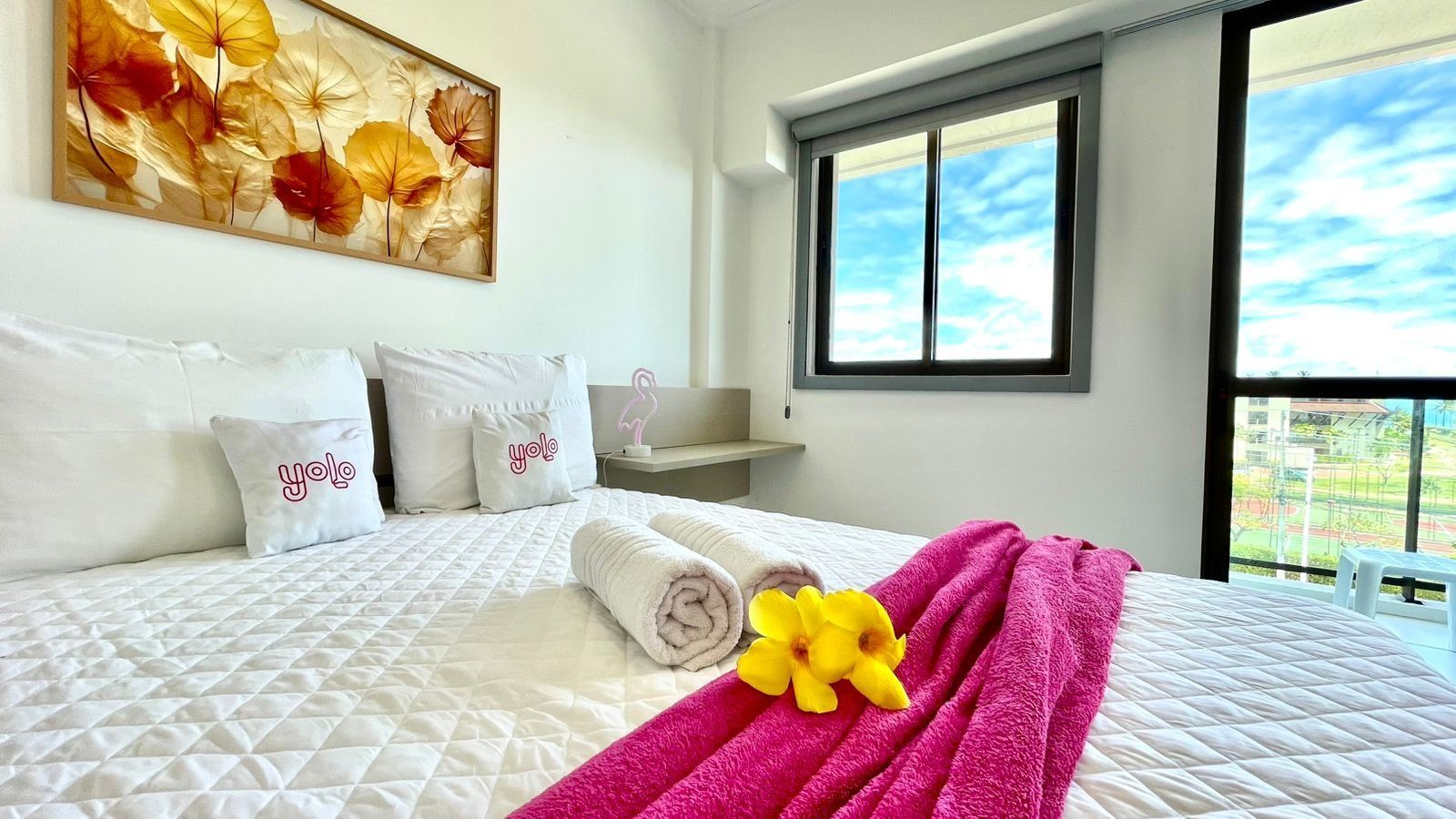 Quarto de hotel com cama, almofadas, janela e vista para o exterior.