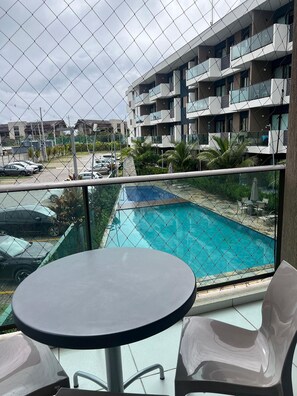 A balcony with a pool view, a table, and chairs. - Makia Beach Experience Porto de Galinhas (Ipojuca)