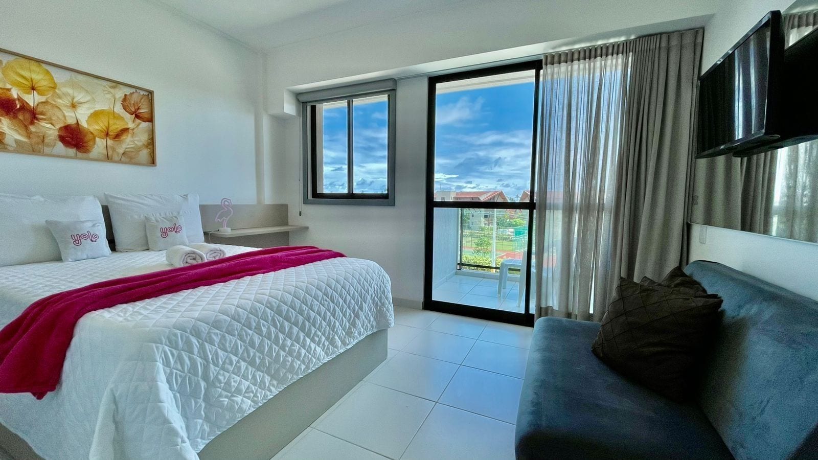 A hotel room with a bed, a sofa, a TV, and a balcony with a view.