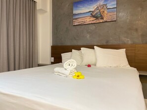 A neatly made bed with white linens, a rolled towel, and a yellow flower. - Makia Beach Experience Porto de Galinhas (Ipojuca)