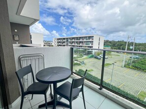 A balcony with a round table and two chairs, overlooking a parking area and a building with multiple balconies. - Makia Beach Experience Porto de Galinhas (Ipojuca)