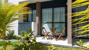 A modern outdoor seating area with a table and two chairs, a large window with curtains, and a palm tree in the foreground. - Makia Beach Experience Porto de Galinhas (Ipojuca)