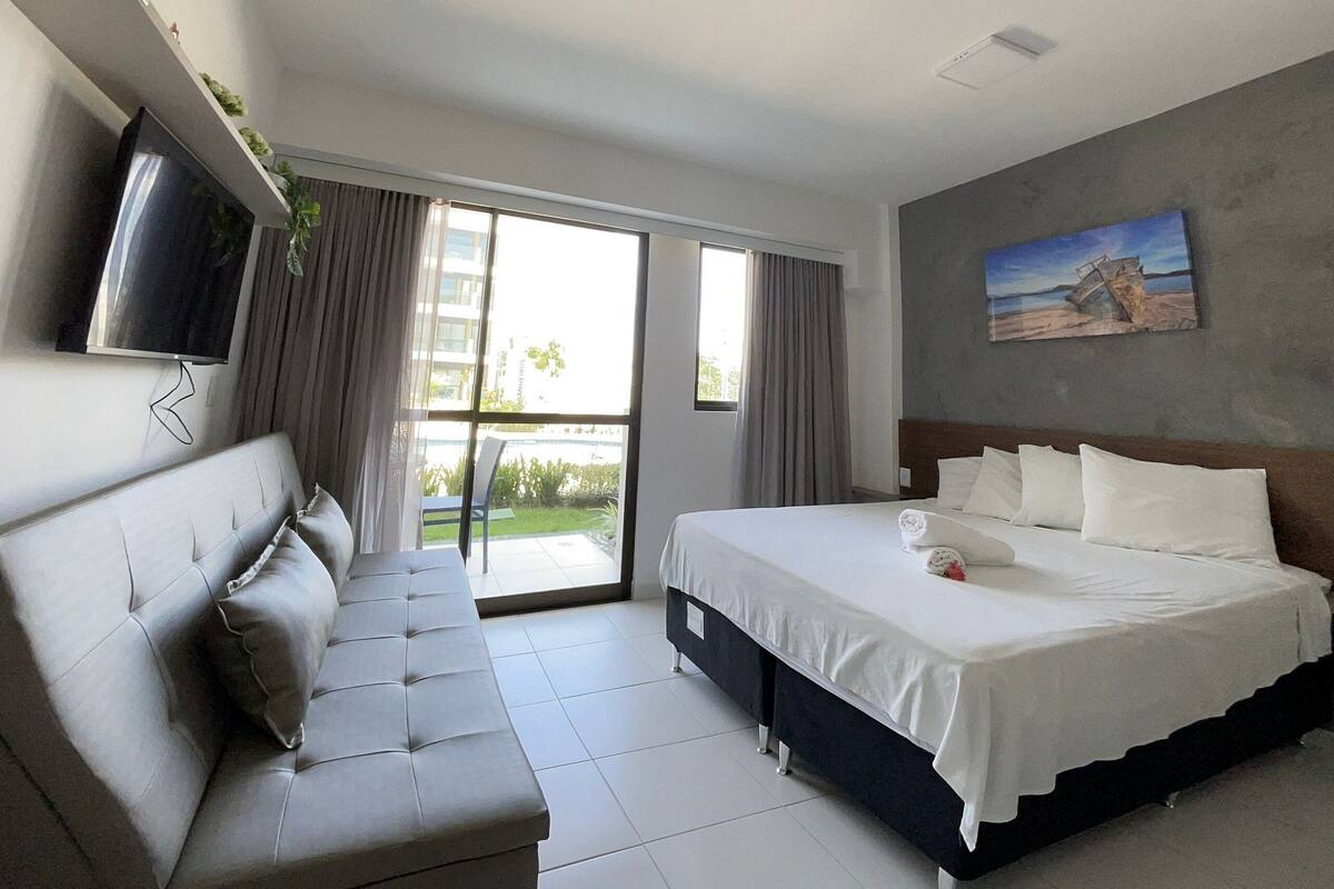 A modern hotel room with a bed, a sofa, a TV, and a painting on the wall.