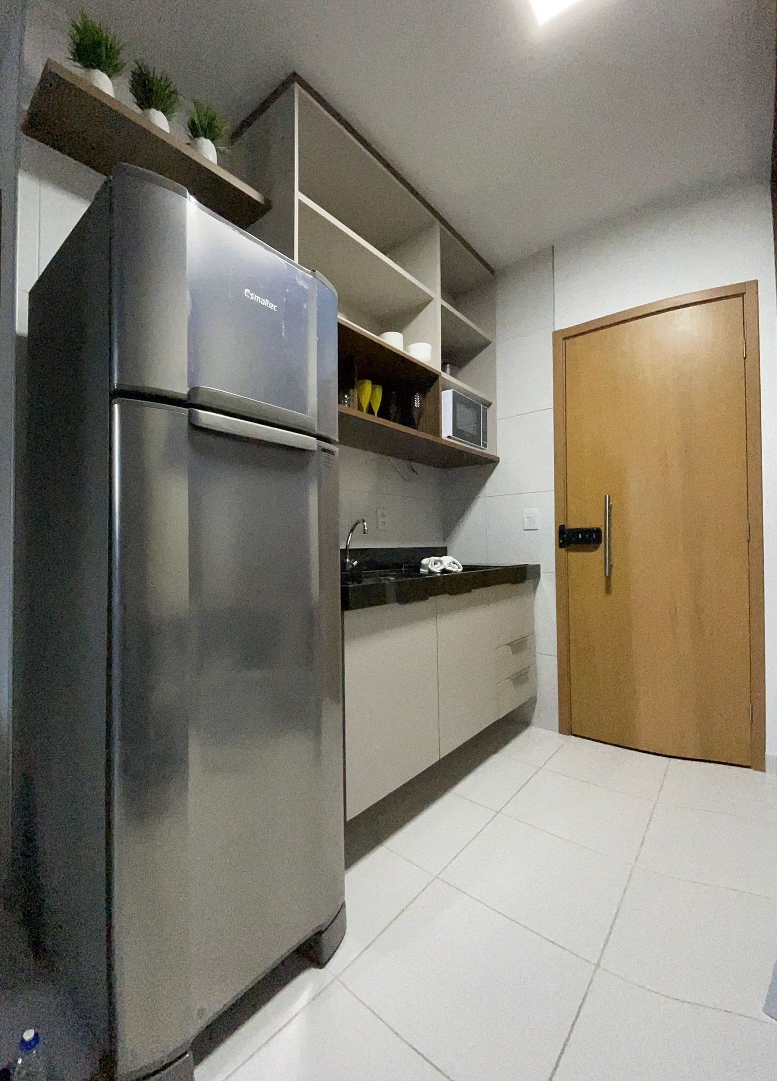 Una cocina compacta con un refrigerador de acero inoxidable, un microondas y una puerta de madera.